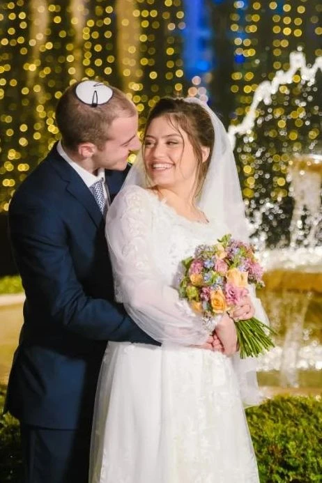 חתן וכלה מחובקים ליד מזרקה מוארת