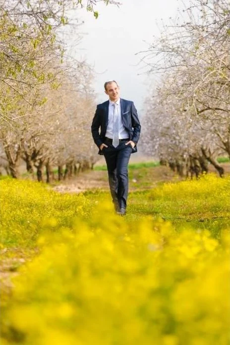 חתן הולך בשביל בין עצי שקד ופרחים צהובים
